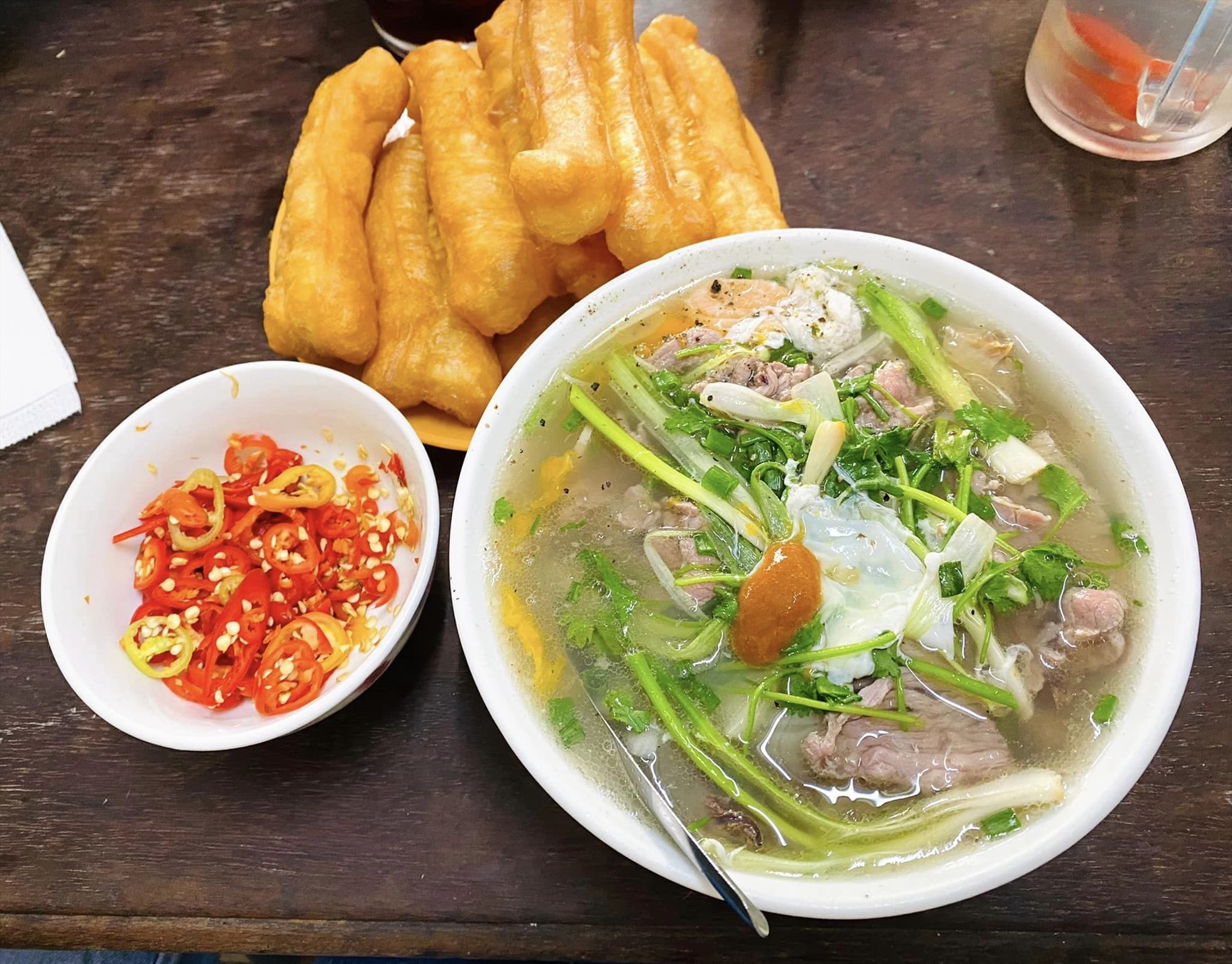 Tô phở bò tái với nước dùng trong, rau thơm, trứng chần, ăn kèm đĩa quẩy và bát ớt tươi thái lát. – Vì sao đến Hà Nội nhiều người muốn thử phở